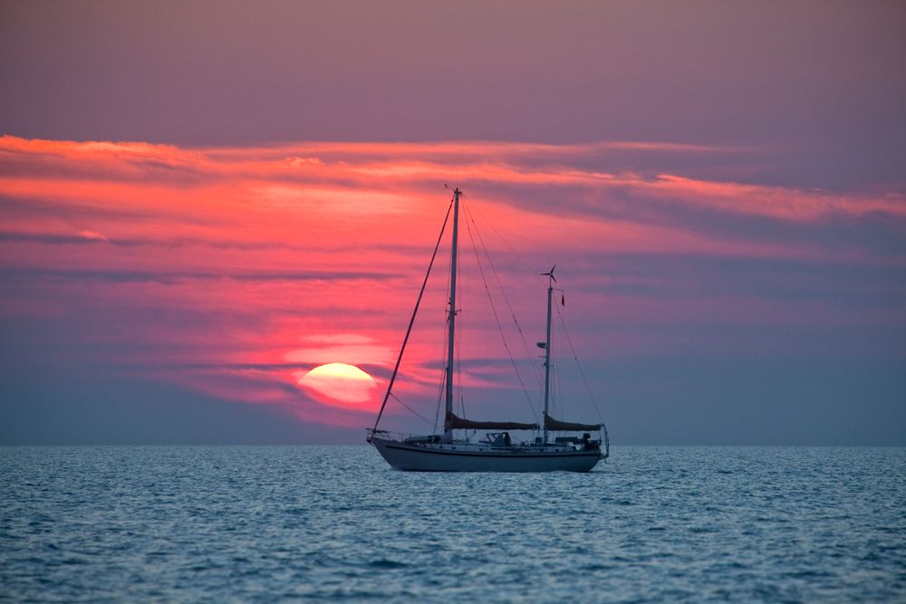 A yatch boat sailing against the vibrant orangish pink sky during sunset at Australian Coastlines
