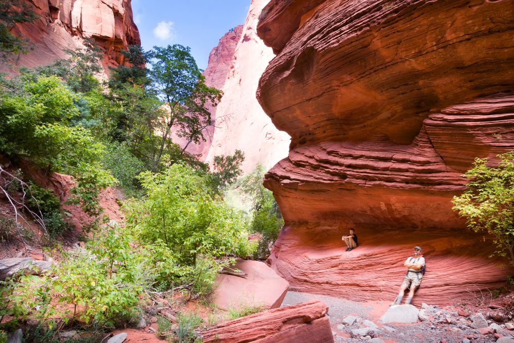Hikers resting on the curves of the red cliffs on their way in Kolob Canyons