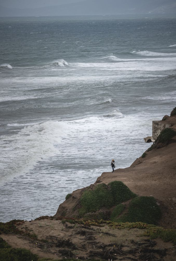 A woman enjoying the waves crashing on the cliffs at Mussel Rock Park