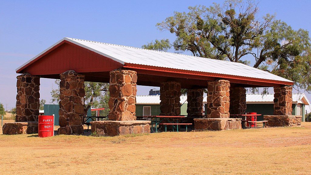Shaded picnic area of Newman Park, with stone posts supporting the red and white coloured roof.