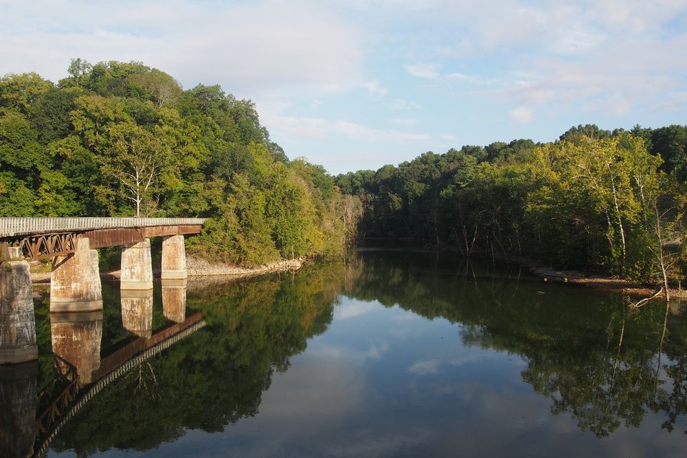 A still body of water reflecting the blue skies and trees around it.