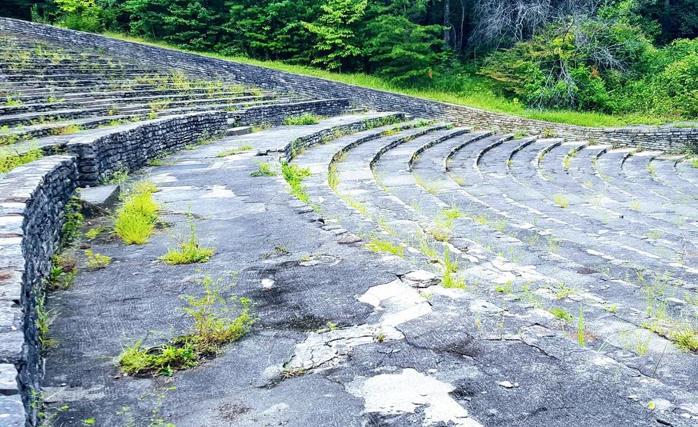 Concrete stone row steps amphitheatre with green trees around it.