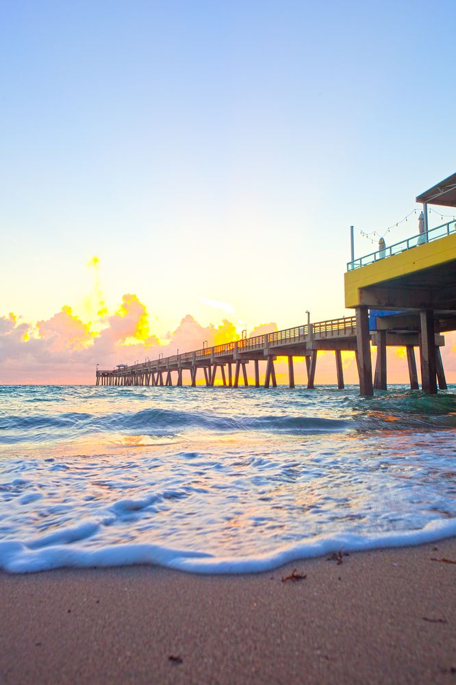 Colorful sunset reflecting on the rushing waves of the beach, and a wooden bridge.