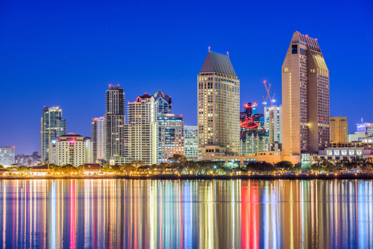 A nighttime view of San Diego, California, showcasing the city’s illuminated skyline reflected on the water.