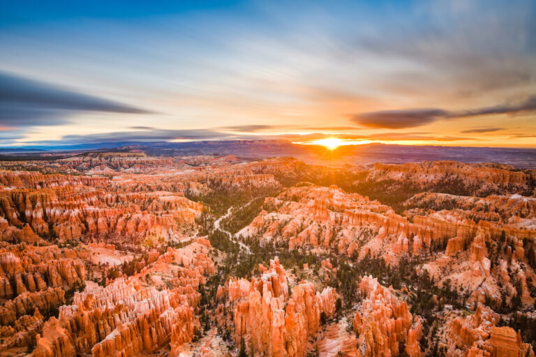 A dawn breaks over Bryce Canyon National Park in Utah, USA, illuminating the intricate rock formations with warm sunlight.