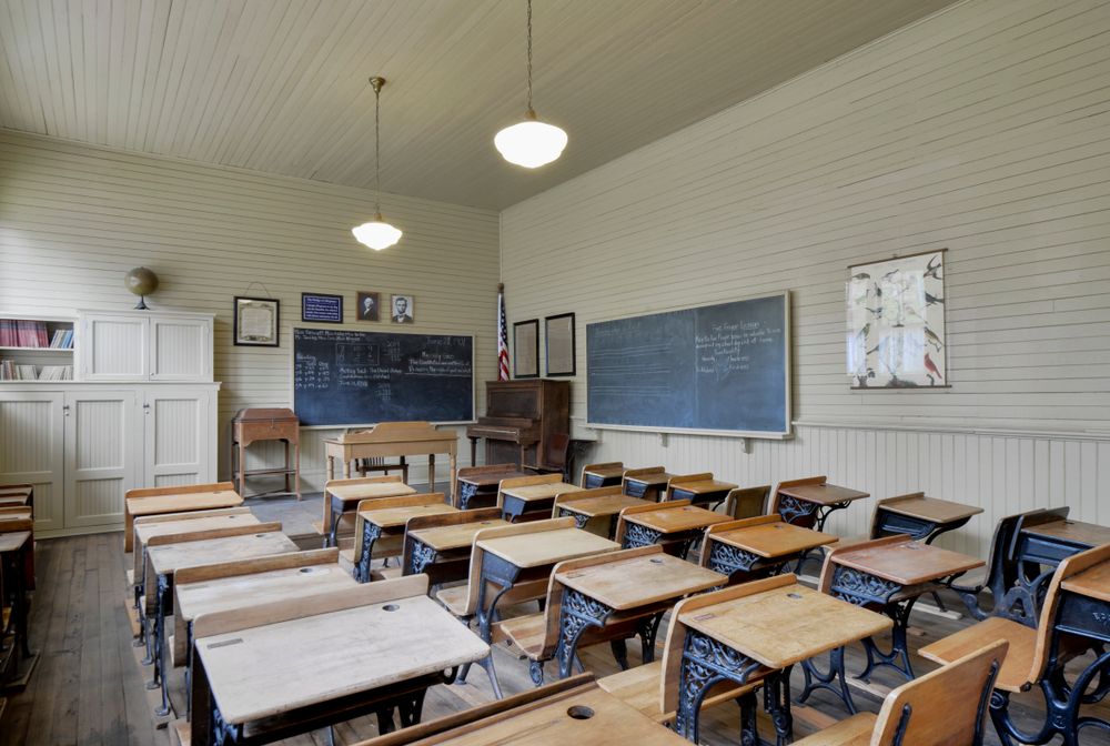 An empty classroom with wooden chairs and matching tables inside the museum.