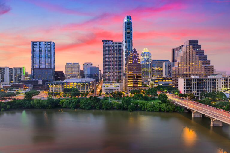 A vibrant sunset sky blankets the downtown skyline of Austin, Texas, USA, with a serene view of the river and the city’s illuminated buildings.