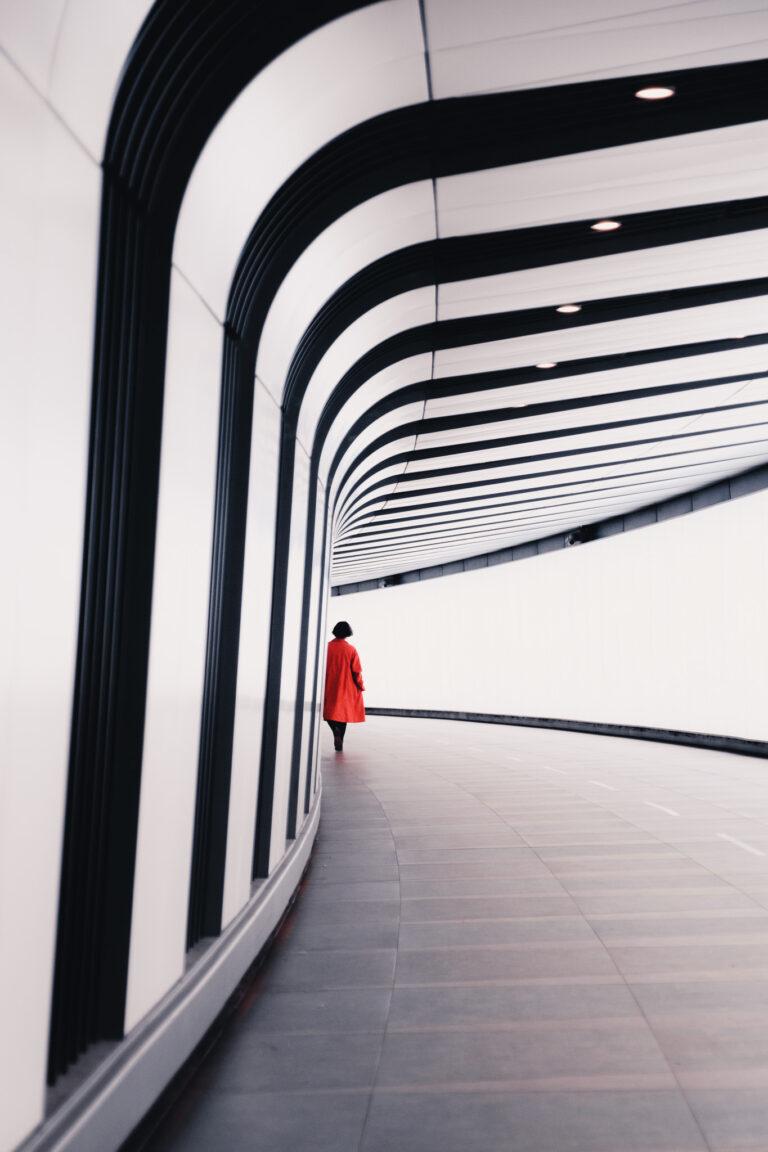 A solitary figure in a striking red coat walks through the sleek curves of a modern London walkway