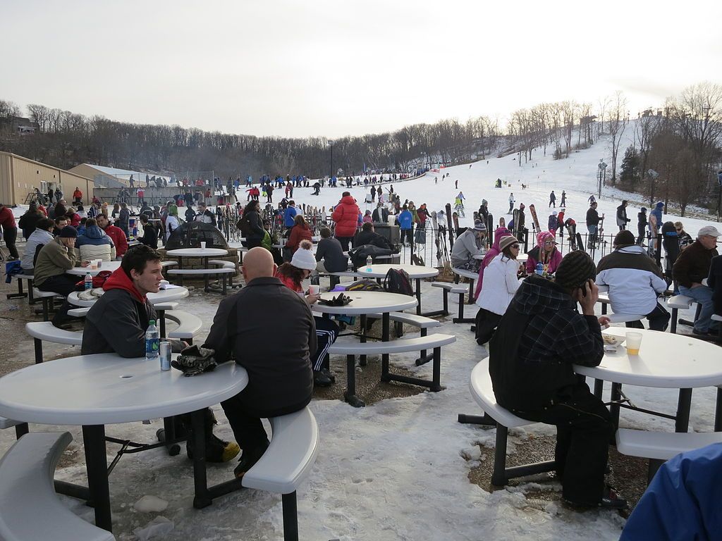 People sitting on the round table and chairs below the ski mountain.