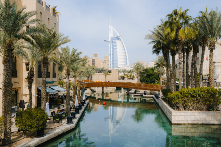 A tranquil waterway lined with palm trees leads the eye towards the iconic Burj Al Arab