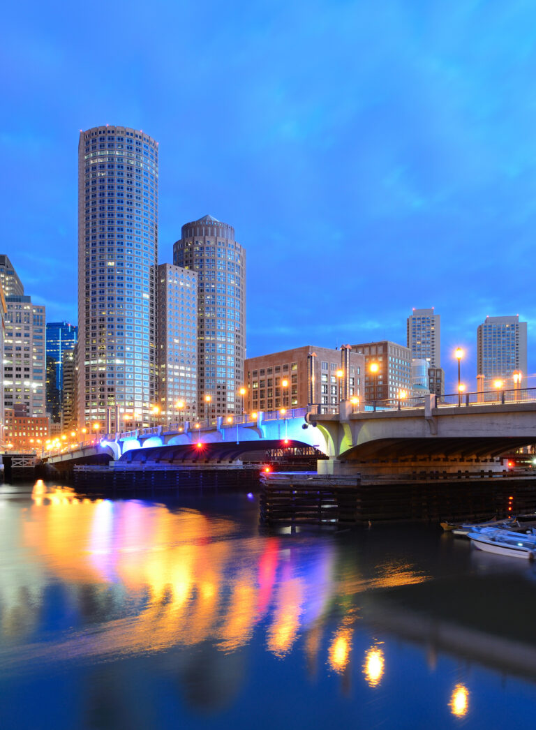 A serene evening view of the Financial District’s skyscrapers in Boston, Massachusetts, reflecting on the calm waters of Boston Harbor.