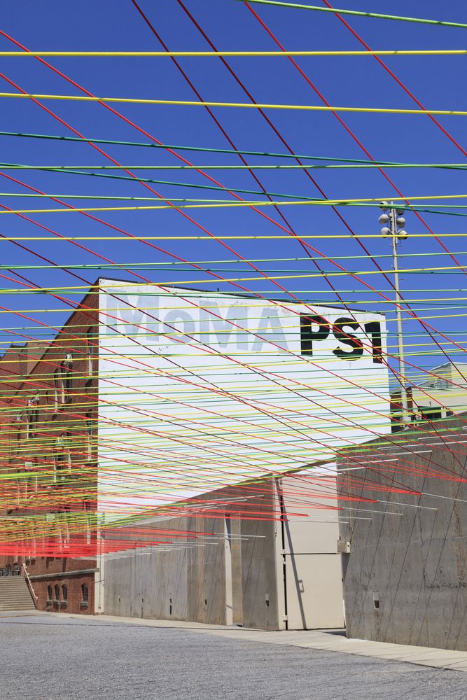 Exterior view of the MoMA PS1 building with colorful wires on the street in front of it.