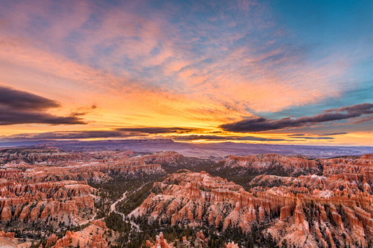 A dawn breaks over Bryce Canyon National Park in Utah, USA, illuminating the hoodoos and rock formations with warm light.