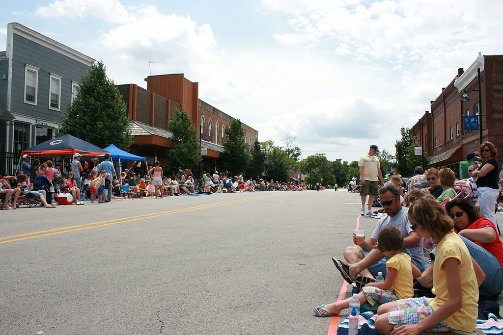 People sitting on a street at Downtown Oswego during a festival