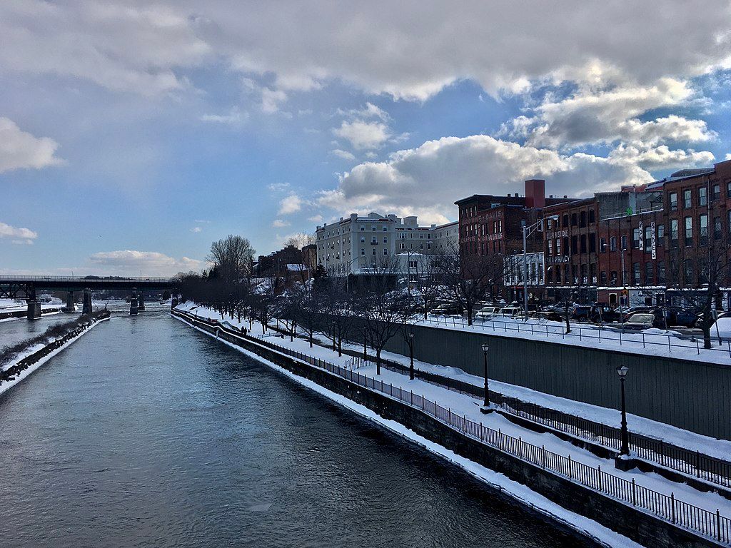 Looking southward along the Oswego River with the bridge covered in snow, and tall buildings standing on the right side.
