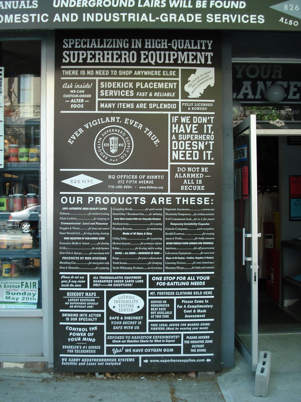 A tall sign post in front of the brooklyn superhero supply - listing their products.