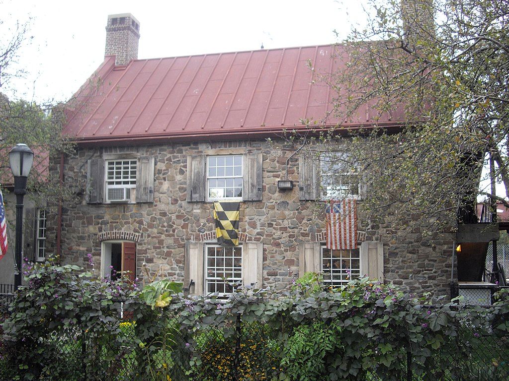 Closer view of the old stone house exterior with two flags hanging from the white glass windows.
