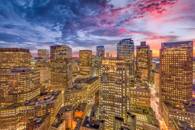 A vibrant dusk sky blankets the financial district skyline of Boston, Massachusetts, USA, showcasing the city’s illuminated buildings.