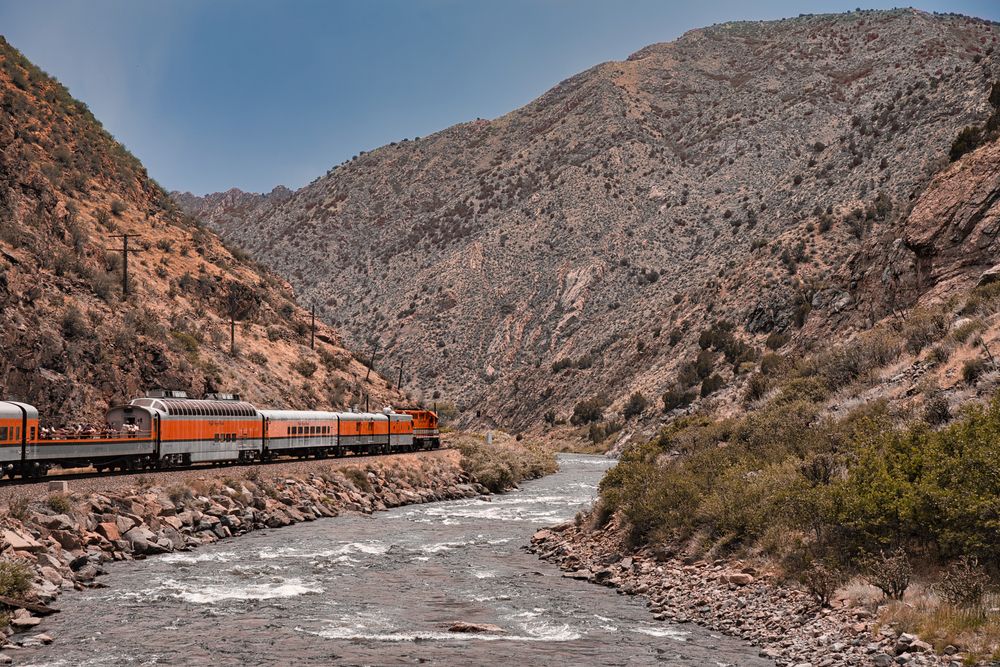 The Royal Gorge Route Railroad train passing by a river and mountains
