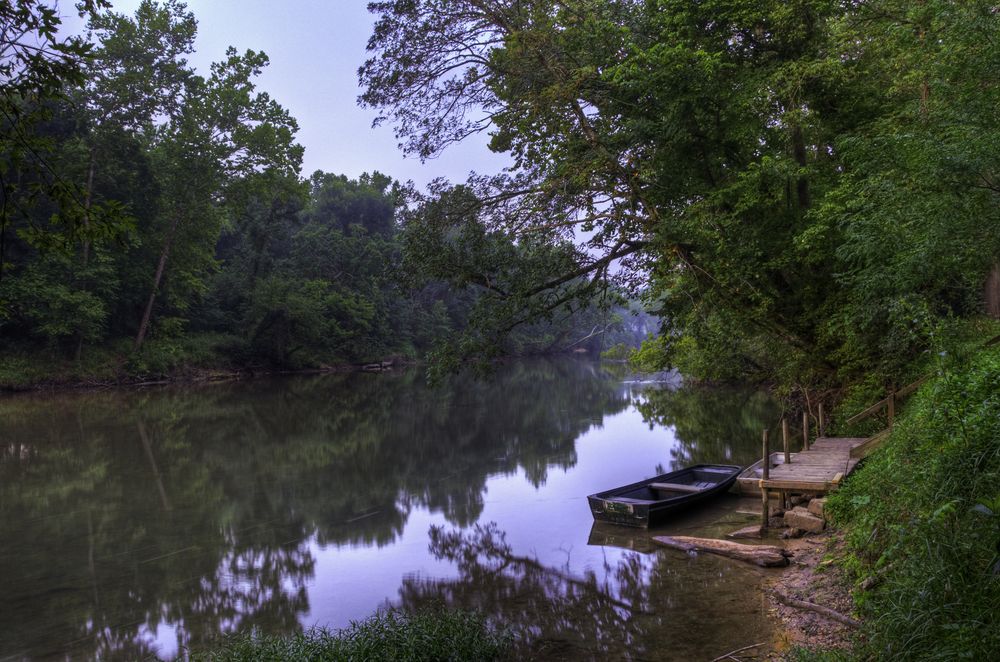 View of the Meramec River waters with an empty boat at the right, and green trees around.