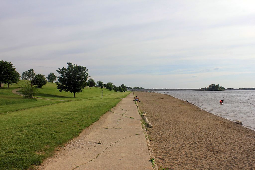 Walkway of buck creek state park with sands near the shore on the right, and grass on the left.