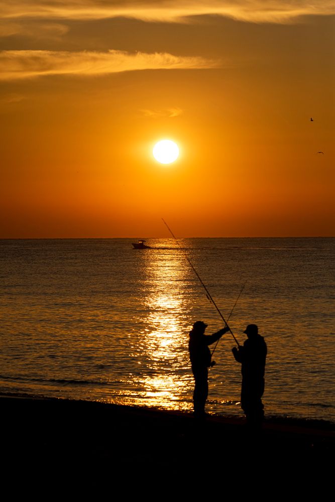Silhouette of two people fishing at the atlantic