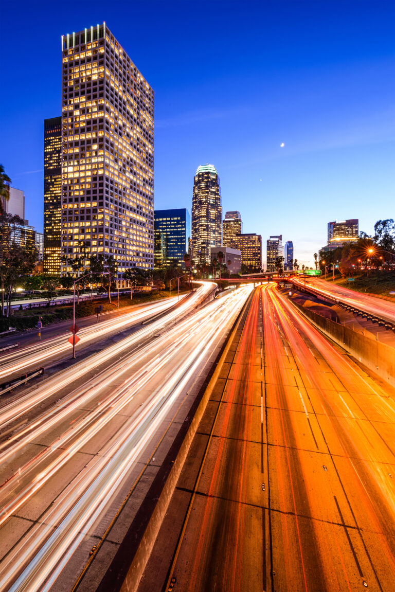 A bustling Los Angeles, California, USA downtown city skyline looms over the streaks of light from the traffic on the highway at dusk.