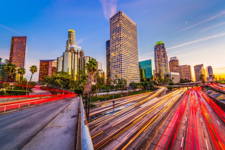 A vibrant evening view of the Los Angeles, California, USA skyline with streaks of light from the bustling highway traffic.