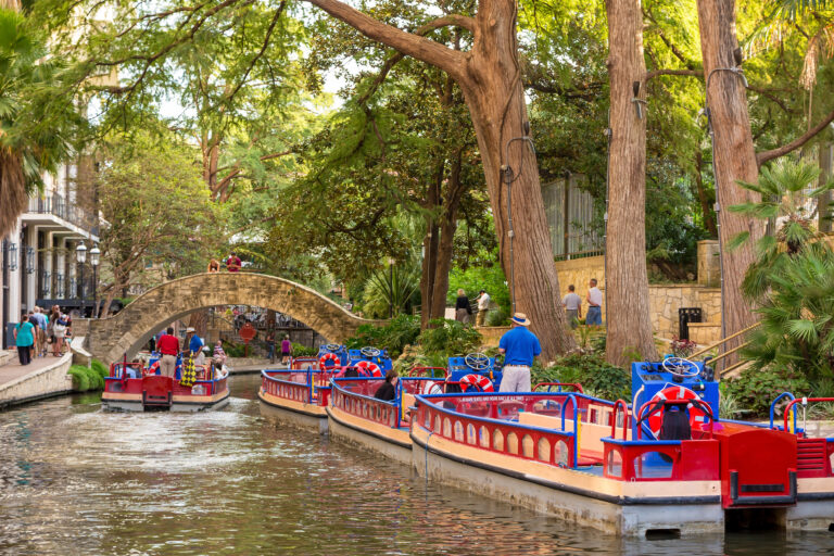 Strolling along the vibrant River Walk in San Antonio, Texas, visitors enjoy a picturesque scene of leisurely boat tours and lush greenery.