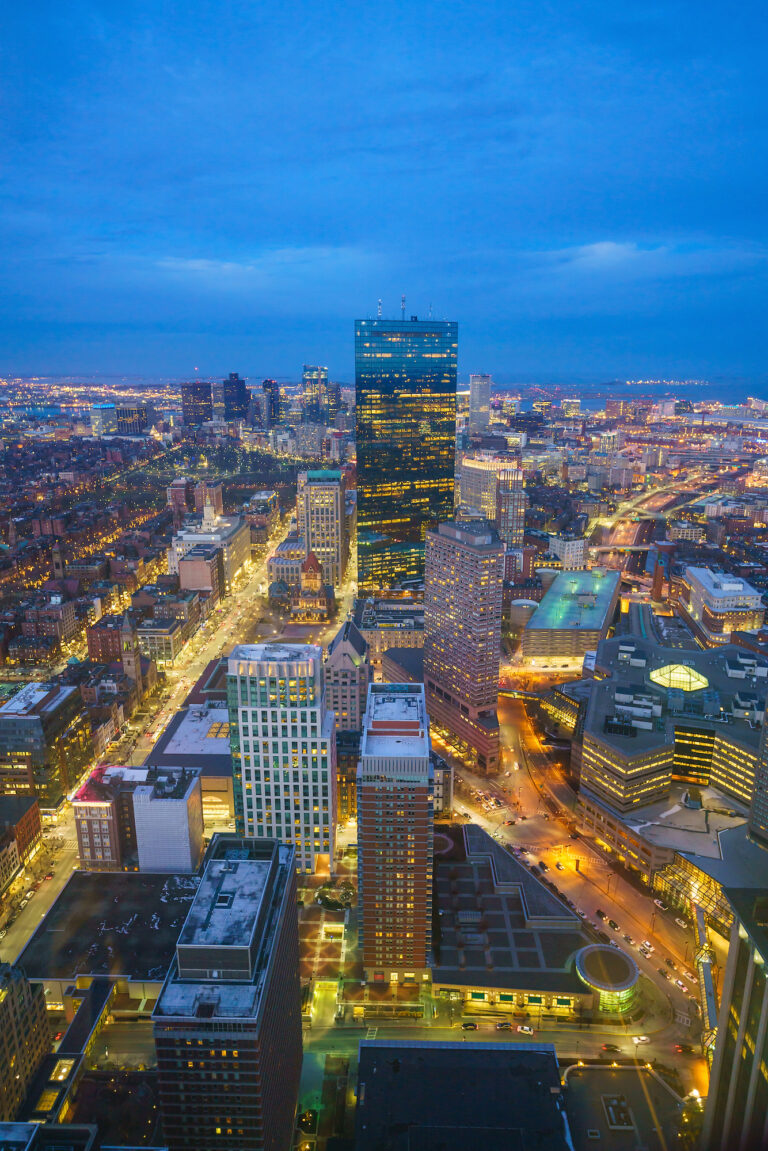Twilight descends on downtown Boston, Massachusetts, as the city lights begin to twinkle against the dusky blue sky.