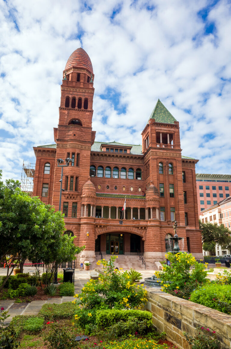 The Bexar County District Court in San Antonio stands majestically under a blue sky, showcasing its historic architecture and the vibrant greenery that surrounds it.