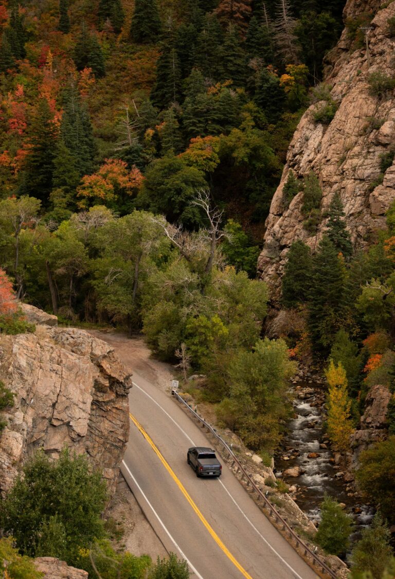 A vehicle meanders along the winding road of Big Cottonwood Canyon, embraced by the vibrant hues of autumn foliage.