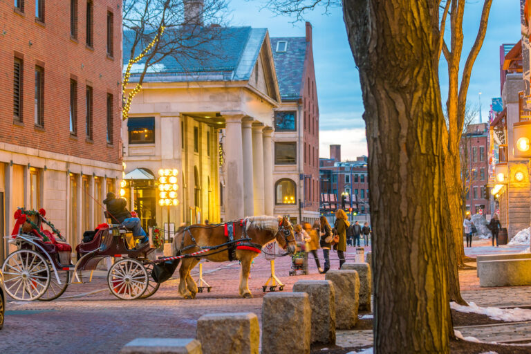 A charming evening view of a historic area in downtown Boston, featuring a horse-drawn carriage and the warm glow of streetlights.