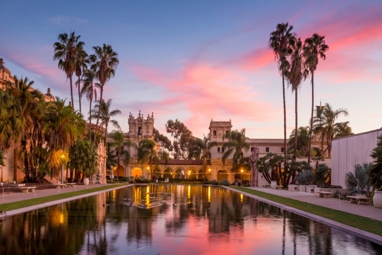 The Casa De Balboa, illuminated by warm lights, basks in the serene glow of a vibrant sunset at Balboa Park in San Diego, USA.