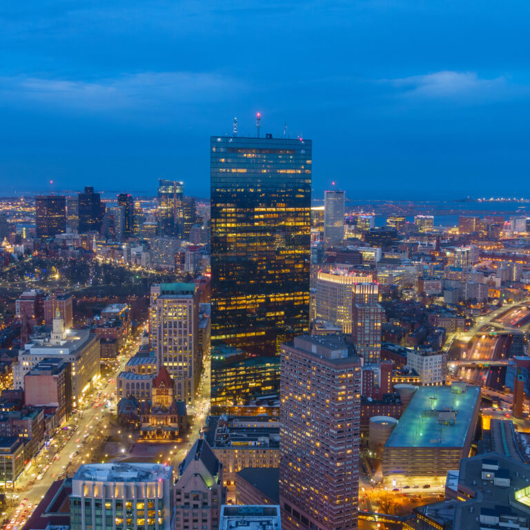 Twilight descends on downtown Boston, Massachusetts, as the city lights begin to twinkle against the dusky blue sky.