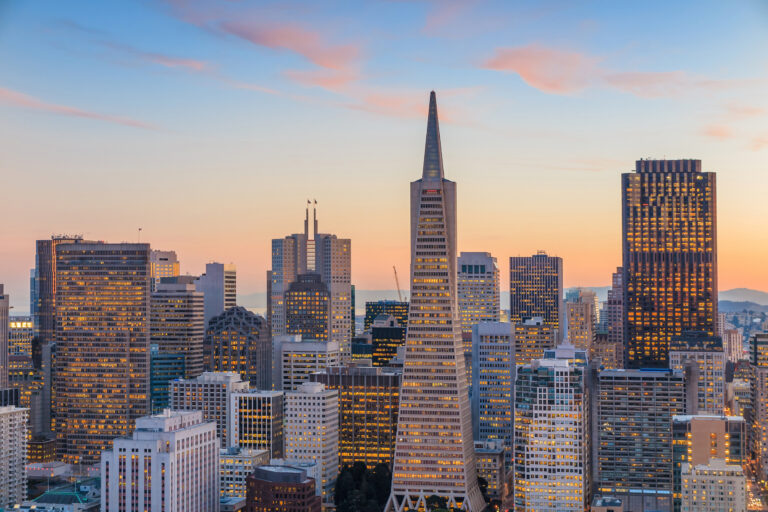 The San Francisco skyline bathes in the warm glow of sunset, showcasing the iconic Transamerica Pyramid amidst the bustling business district.