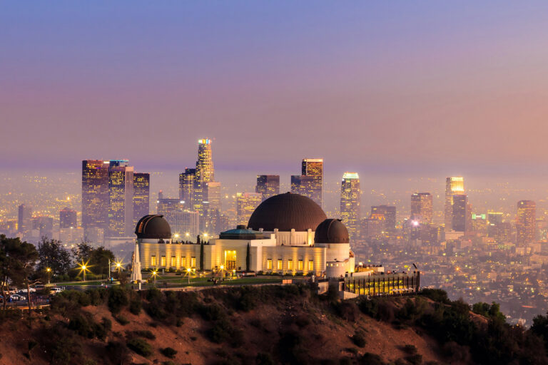 The Griffith Observatory stands sentinel before the sprawling Los Angeles skyline as the city lights twinkle under a dusky sky.