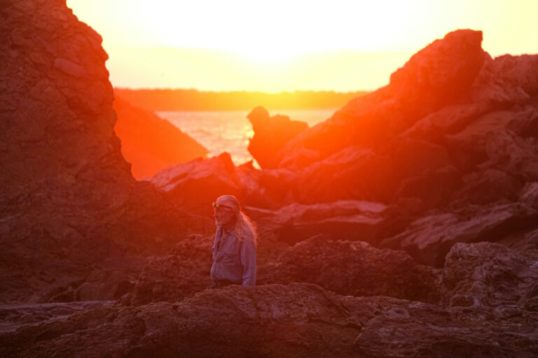 A serene sunset bathes Little Corona del Mar Beach in warm hues as a person enjoys the tranquil beauty of the coastal landscape.