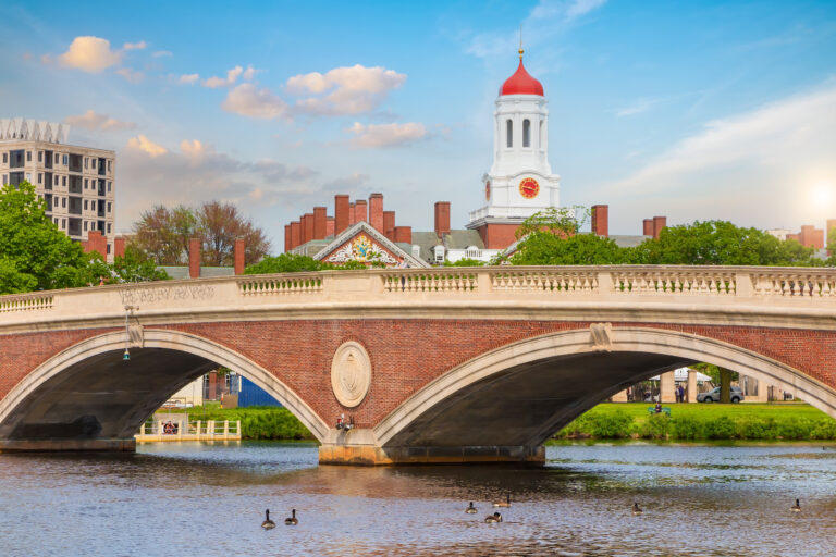 The John W. Weeks Bridge, adorned with a distinctive clock tower, gracefully arches over the Charles River against the backdrop of Harvard University’s historic campus in Boston.