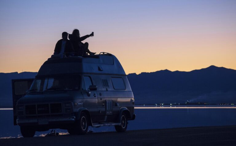Friends share a serene moment atop a van as the day fades into a tranquil dusk at the Bonneville Salt Flats in Utah.