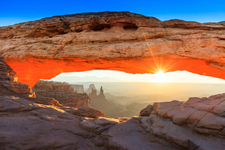 The golden rays of sunrise frame the iconic Mesa Arch in Canyonlands National Park, illuminating the vast and rugged landscape below.
