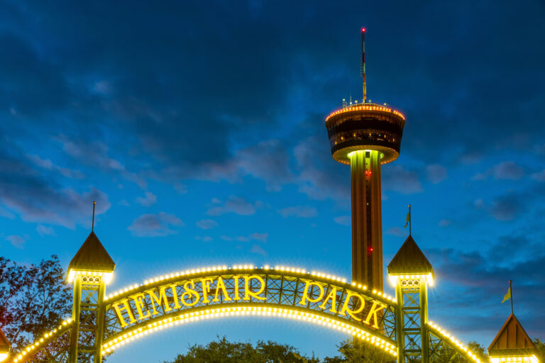 The Tower of the Americas stands tall against the evening sky, illuminated by the vibrant lights of Hemisfair Park in San Antonio.