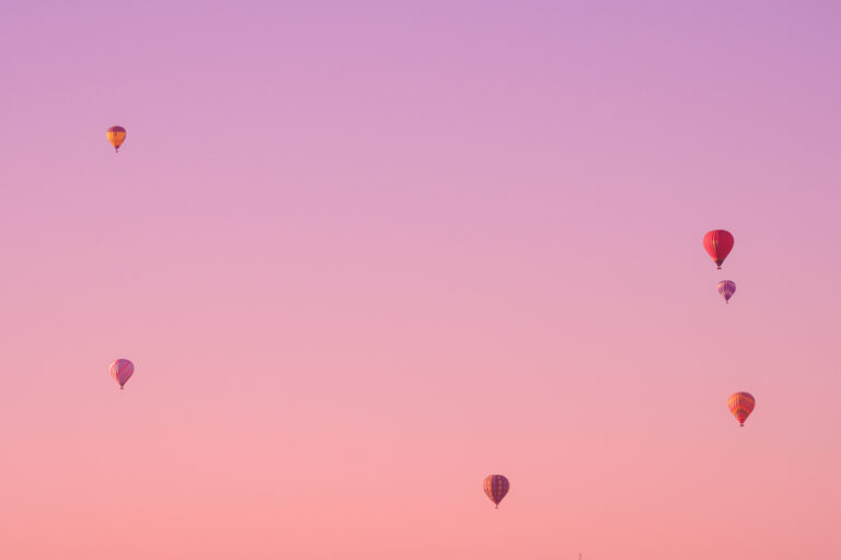 Colorful hot air balloons float serenely over Temecula Valley against a pastel-hued sunset sky.