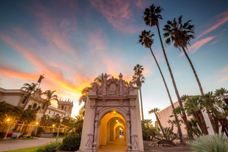 A serene sunset paints the sky with warm hues over the historic architecture of Balboa Park in San Diego, California.