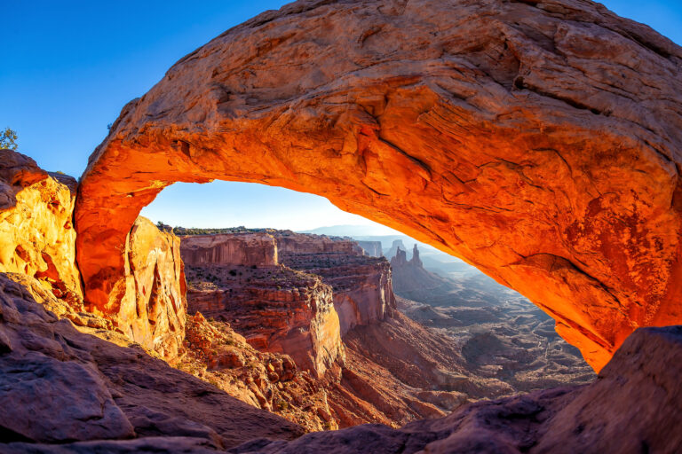 The warm glow of sunrise illuminates Mesa Arch, creating a stunning natural window to the vast Canyonlands National Park in Utah, USA.